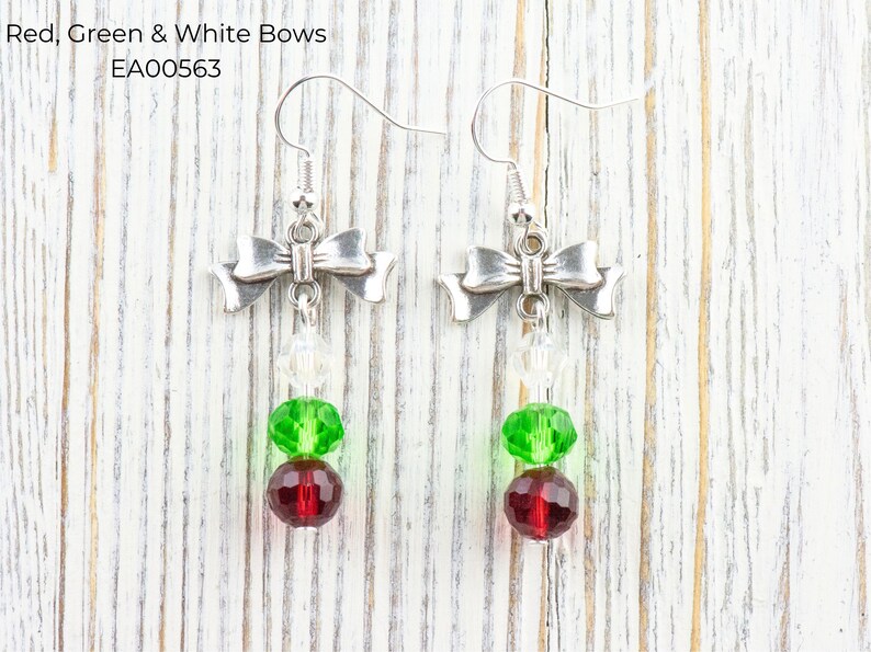 Pode incluir: Brincos de la&ccedil;o prateados com contas vermelhas, verdes e transparentes. Os brincos apresentam um design de la&ccedil;o na parte superior, com contas vermelhas, verdes e transparentes penduradas abaixo. O texto "Red, Green & White Bows" est&aacute; na imagem.
