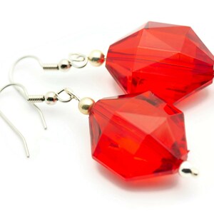 May include: A pair of red crystal earrings with silver hooks. The crystals are faceted and have a geometric shape.