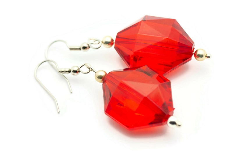 May include: A pair of red crystal earrings with silver hooks. The crystals are faceted and have a geometric shape.