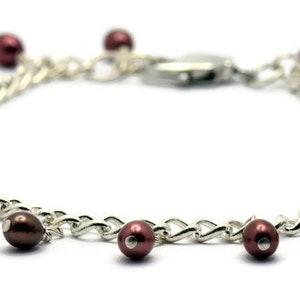 May include: A silver chain bracelet with a silver clasp and multiple dangling maroon pearls.