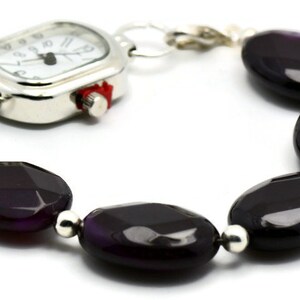 May include: A silver watch with a square face and a black agate bead bracelet. The watch has a white face with black hands and numbers.