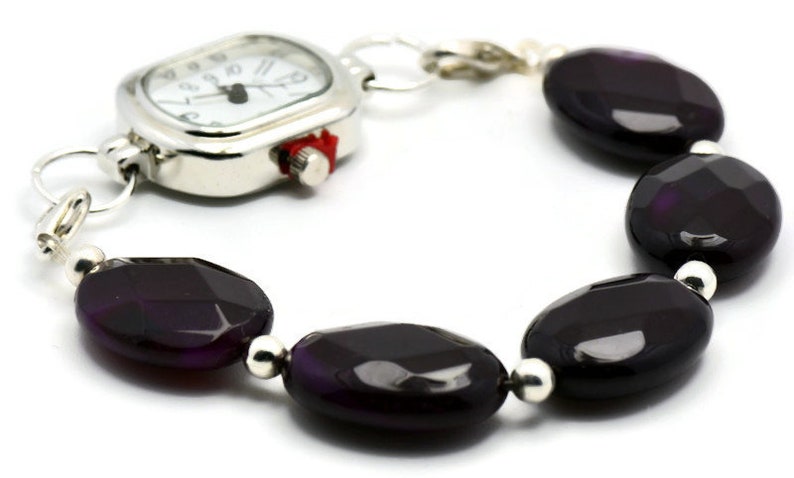 May include: A silver watch with a square face and a black agate bead bracelet. The watch has a white face with black hands and numbers.