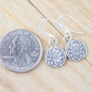 May include: A pair of silver dangle earrings with a delicate floral design. The earrings are about the size of a quarter.