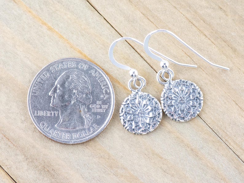 May include: A pair of silver dangle earrings with a delicate floral design. The earrings are about the size of a quarter.