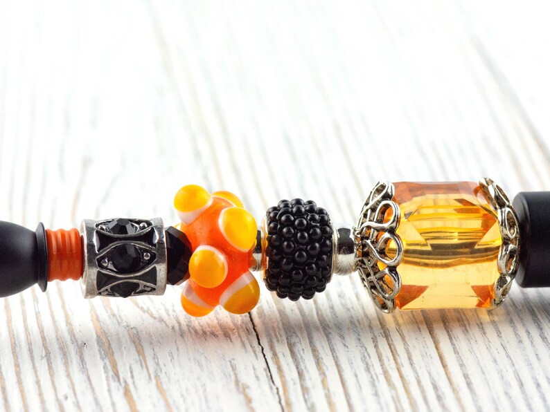 May include: A black and orange beaded bracelet with various decorative beads. The beads include a silver bead with black accents, an orange and yellow bead, a black textured bead, and a large amber-colored bead with a silver filigree setting.
