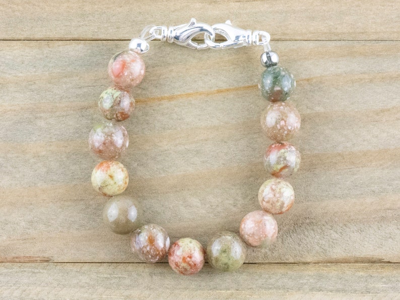 Pu&ograve; includere: Un braccialetto con grandi perline rotonde e macchiate, nei toni del rosa, verde e beige. Il braccialetto &egrave; chiuso da una chiusura argentata. Le perline, di circa 1,5 cm di diametro, hanno un aspetto naturale, forse pietra preziosa o minerale.