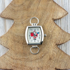 May include: A silver square watch with a white face and a Santa Claus design. The watch is on a wooden Christmas tree cutout.