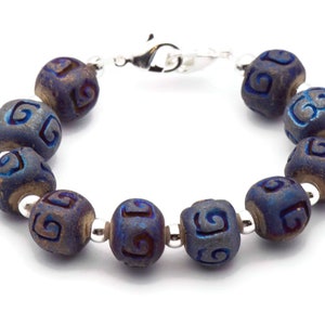 Pu&ograve; includere: Un braccialetto blu e argento con una chiusura argentata. Il braccialetto &egrave; fatto di perline rotonde con un motivo a spirale.