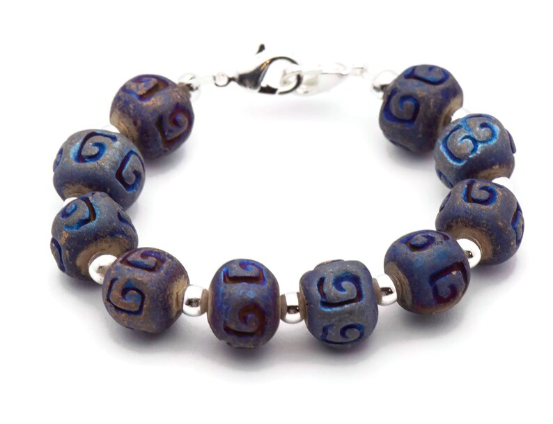 Pu&ograve; includere: Un braccialetto blu e argento con una chiusura argentata. Il braccialetto &egrave; fatto di perline rotonde con un motivo a spirale.
