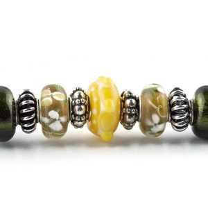 Peut inclure: Gros plan sur un bracelet &agrave; breloques avec une vari&eacute;t&eacute; de perles en verre dans des tons de vert, marron et jaune. Les perles sont entrecoup&eacute;es d'entretoises argent&eacute;es.