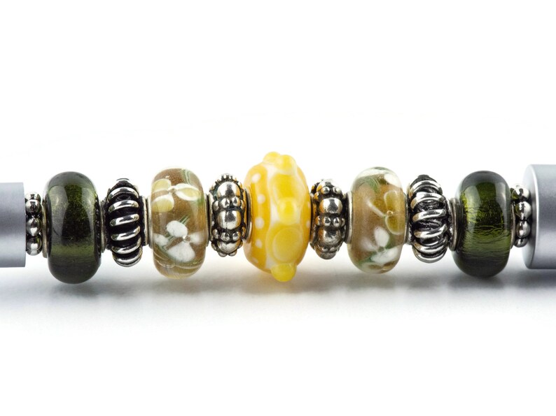 Peut inclure: Gros plan sur un bracelet &agrave; breloques avec une vari&eacute;t&eacute; de perles en verre dans des tons de vert, marron et jaune. Les perles sont entrecoup&eacute;es d'entretoises argent&eacute;es.