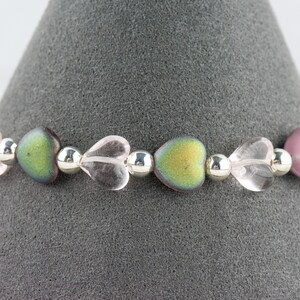 May include: A bracelet made with alternating clear heart-shaped beads, iridescent green heart-shaped beads, and silver beads.
