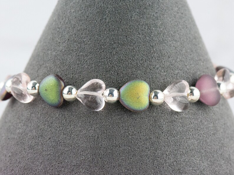 May include: A bracelet made with alternating clear heart-shaped beads, iridescent green heart-shaped beads, and silver beads.