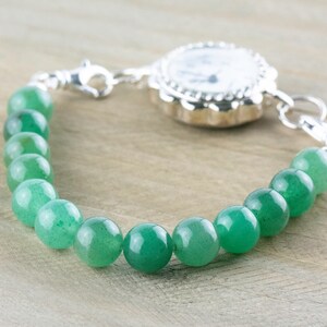 May include: A silver watch bracelet with a green stone bead chain. The watch face is white with black markings.