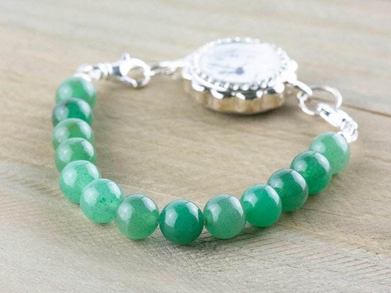May include: A silver watch bracelet with a green stone bead chain. The watch face is white with black markings.