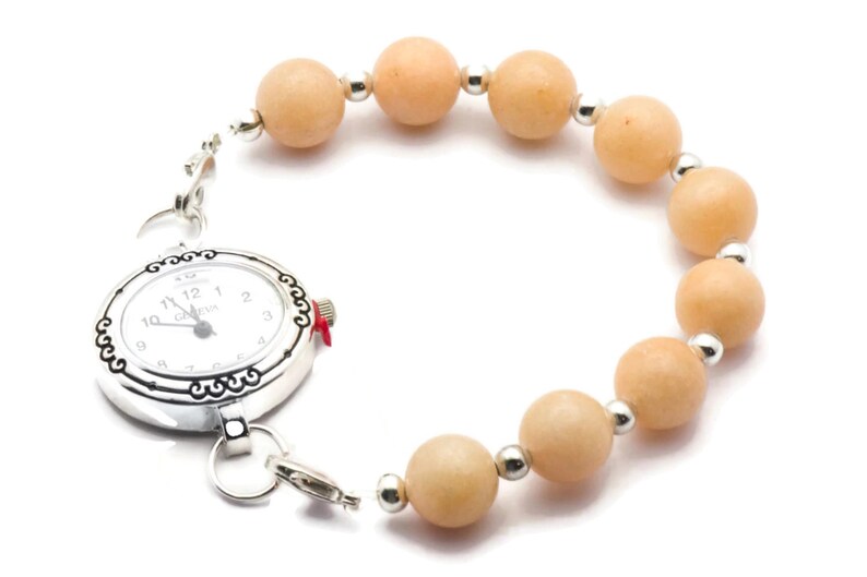 Puede incluir: Un reloj plateado con una esfera blanca y n&uacute;meros negros est&aacute; unido a una pulsera hecha de cuentas de color naranja claro.