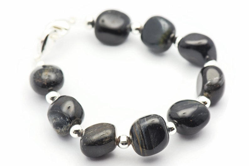 K&ouml;nnte beinhalten: Armband aus schwarzen Edelsteinen mit silbernen Perlen und einem Verschluss. Das Armband besteht aus glatten, ovalen Steinen.