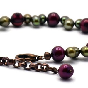 May include: A bracelet made of green and burgundy pearls with a copper clasp.
