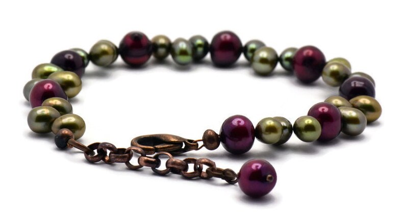 May include: A bracelet made of green and burgundy pearls with a copper clasp.