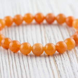 May include: A bracelet made of orange carnelian beads. The beads are round and smooth, and the bracelet is strung on a clear elastic cord.