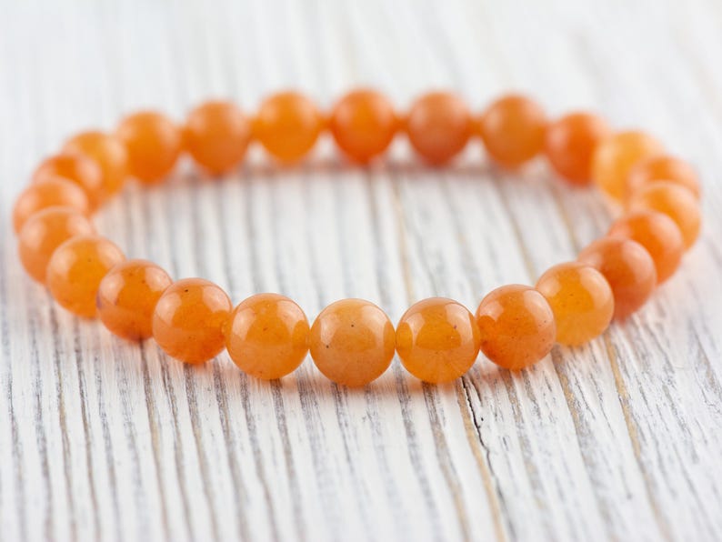 May include: A bracelet made of orange carnelian beads. The beads are round and smooth, and the bracelet is strung on a clear elastic cord.
