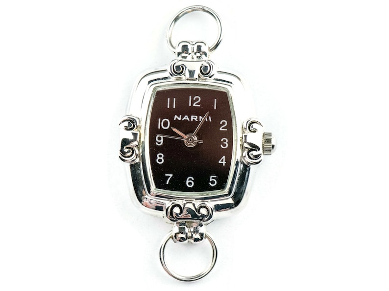 Pu&ograve; includere: Orologio rettangolare argentato con quadrante marrone scuro, numeri e lancette bianche. L'orologio ha una cornice decorativa e due attacchi ad anello. Il marchio "NARMI" &egrave; stampato sul quadrante.