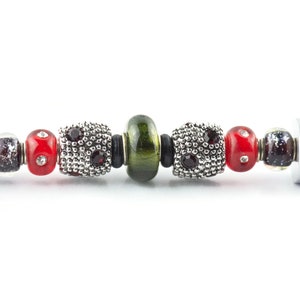 May include: A silver charm bracelet with red, green and black beads. The beads are made of glass and metal.