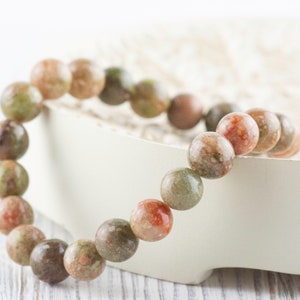 May include: A bracelet made of round, multi-colored, green, pink, and brown stones.