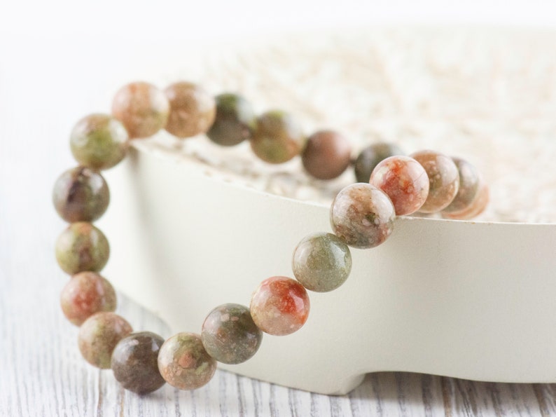 May include: A bracelet made of round, multi-colored, green, pink, and brown stones.