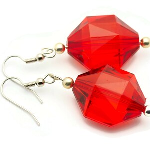 May include: A pair of red crystal earrings with silver hooks. The crystals are faceted and have a geometric shape.