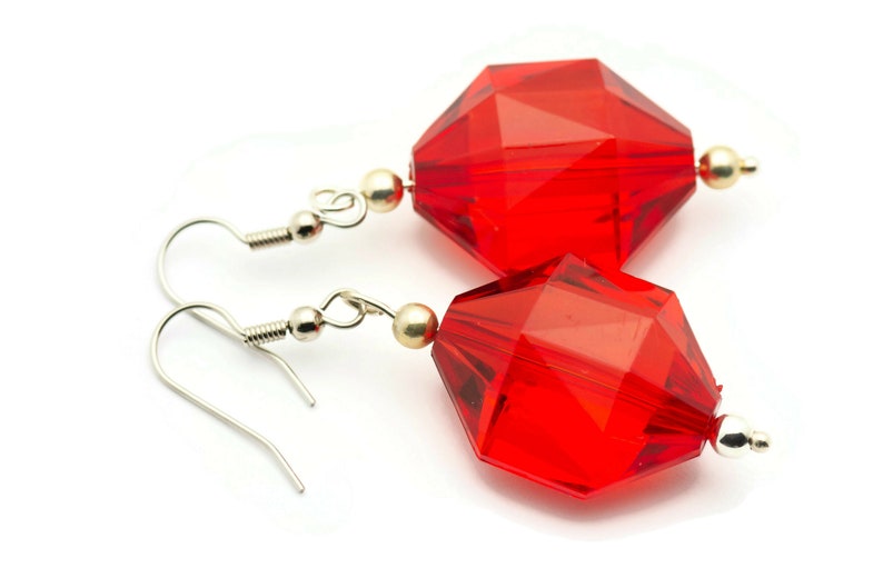 May include: A pair of red crystal earrings with silver hooks. The crystals are faceted and have a geometric shape.