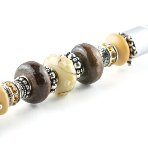 May include: A silver stylus pen with a decorative beaded design. The beads are brown, cream, and gold with silver accents.