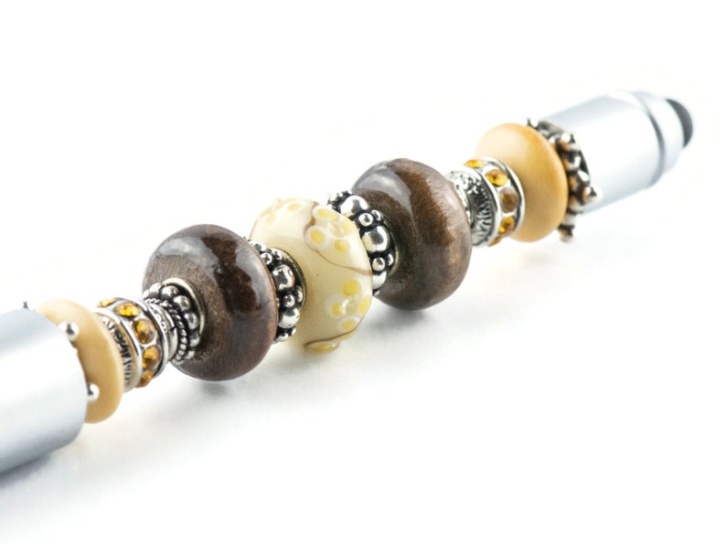 May include: A silver stylus pen with a decorative beaded design. The beads are brown, cream, and gold with silver accents.