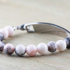 May include: A silver bracelet with a personalised tag and pink and grey marbled beads.