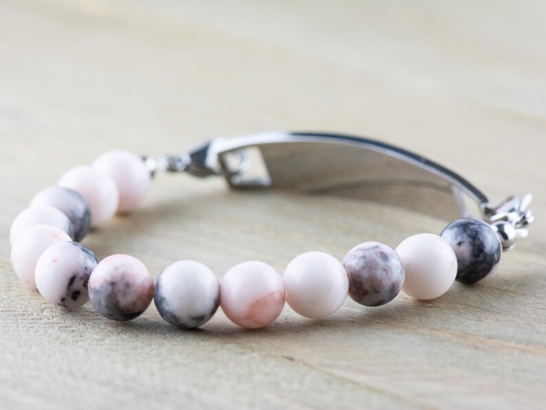 May include: A silver bracelet with a personalised tag and pink and grey marbled beads.