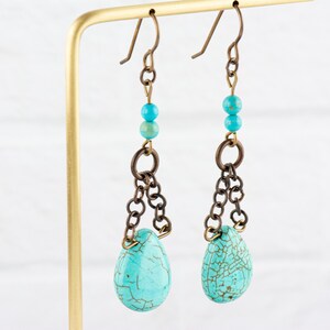 May include: Turquoise teardrop earrings with a chain and bead accents. The earrings are made of brass and turquoise.
