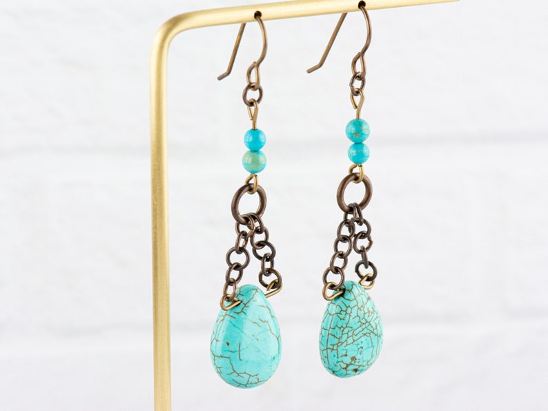 May include: Turquoise teardrop earrings with a chain and bead accents. The earrings are made of brass and turquoise.