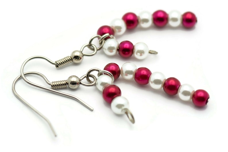 May include: A pair of silver dangle earrings with white and red beads. The beads are arranged in a candy cane pattern.