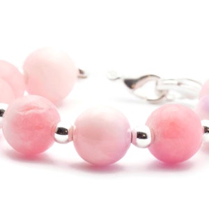 Puede incluir: Una pulsera de cuentas rosas con cierre plateado. La pulsera presenta una serie de cuentas redondas de color rosa claro con detalles plateados. Las cuentas var&iacute;an en tonalidad de rosa claro a medio.