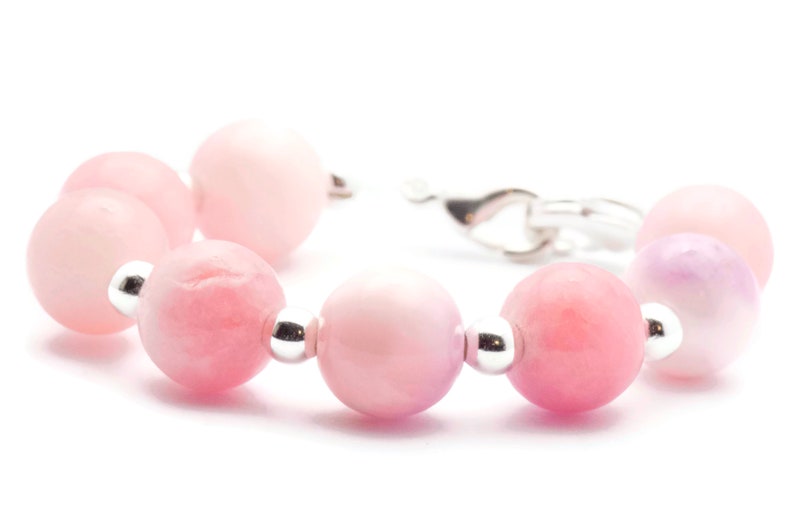Puede incluir: Una pulsera de cuentas rosas con cierre plateado. La pulsera presenta una serie de cuentas redondas de color rosa claro con detalles plateados. Las cuentas var&iacute;an en tonalidad de rosa claro a medio.