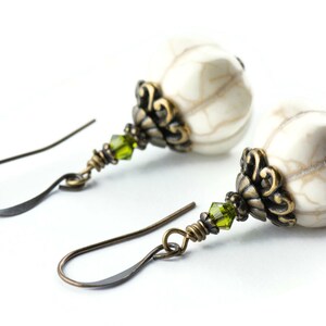 May include: A pair of earrings featuring white howlite stone beads, green crystal accents, and antique brass filigree.