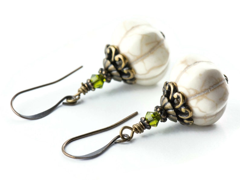 May include: A pair of earrings featuring white howlite stone beads, green crystal accents, and antique brass filigree.