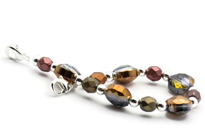 K&ouml;nnte beinhalten: Ein Armband mit silbernem Verschluss und braunen, goldenen und klaren Glasperlen.