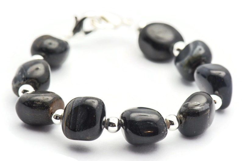 K&ouml;nnte beinhalten: Ein Armband aus schwarzen Edelsteinen mit silbernen Perlen und einem Verschluss. Das Armband besteht aus glatten, abgerundeten Steinen.