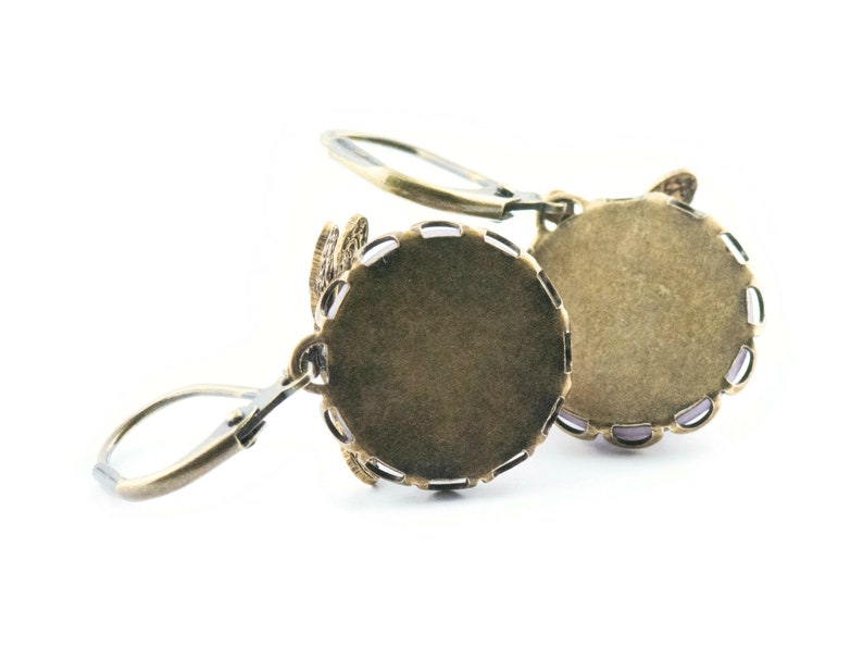 Pode incluir: Um par de engastes para brincos de cor bronze com um design de filigrana decorativo. Os engastes s&atilde;o redondos e t&ecirc;m um acabamento liso e polido.