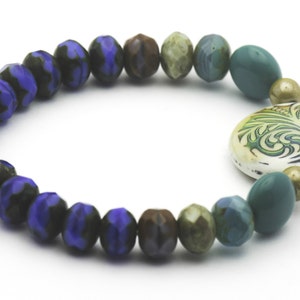 Puede incluir: Un brazalete de cuentas azules, verdes y marrones con un dije de cer&aacute;mica blanca con un dise&ntilde;o floral verde.