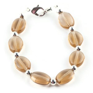 May include: A brown glass bead bracelet with silver accents. The bracelet is made of oval-shaped beads and has a silver clasp.