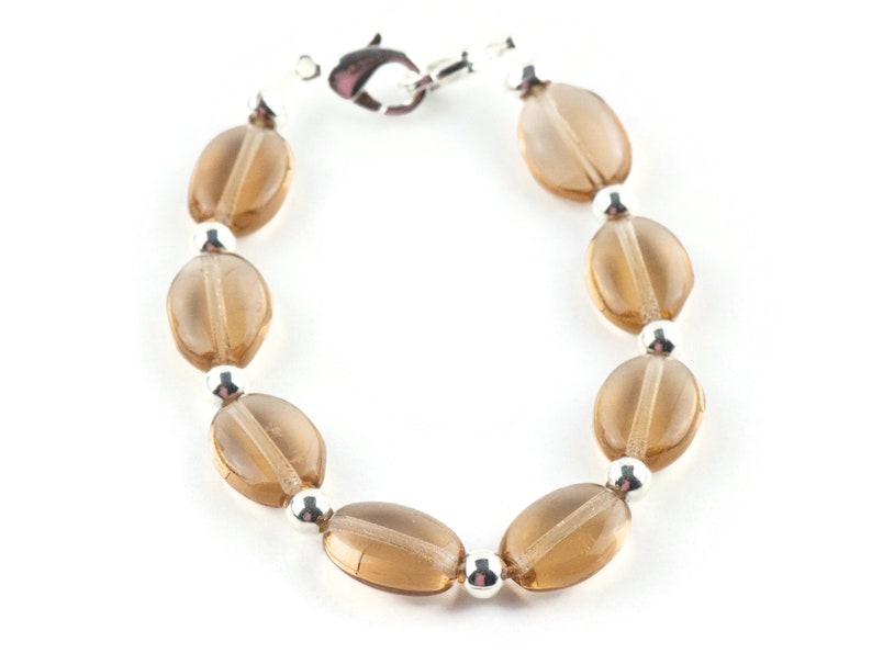 May include: A brown glass bead bracelet with silver accents. The bracelet is made of oval-shaped beads and has a silver clasp.