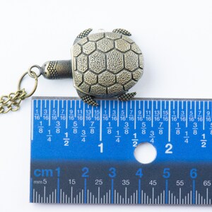 May include: A bronze turtle pendant necklace with a chain. The turtle is about 1 1/2 inches wide. The pendant is measured against a ruler.