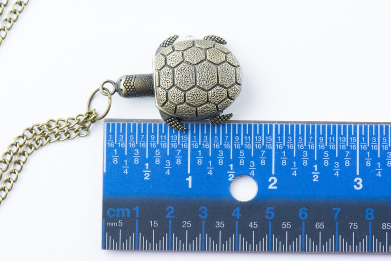 May include: A bronze turtle pendant necklace with a chain. The turtle is about 1 1/2 inches wide. The pendant is measured against a ruler.
